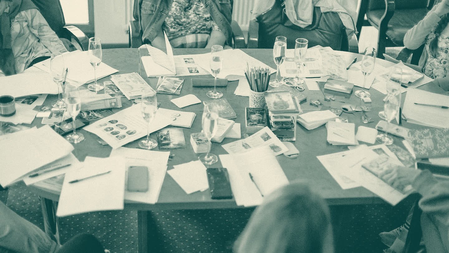 A round table covered in cards, printed sheets and notes, with participants seated around it.