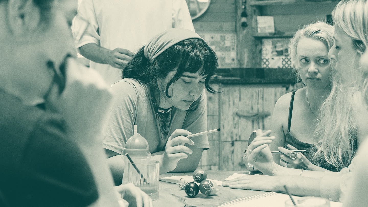 Adults around a table with pens, notes and small game pieces, deep in conversation.